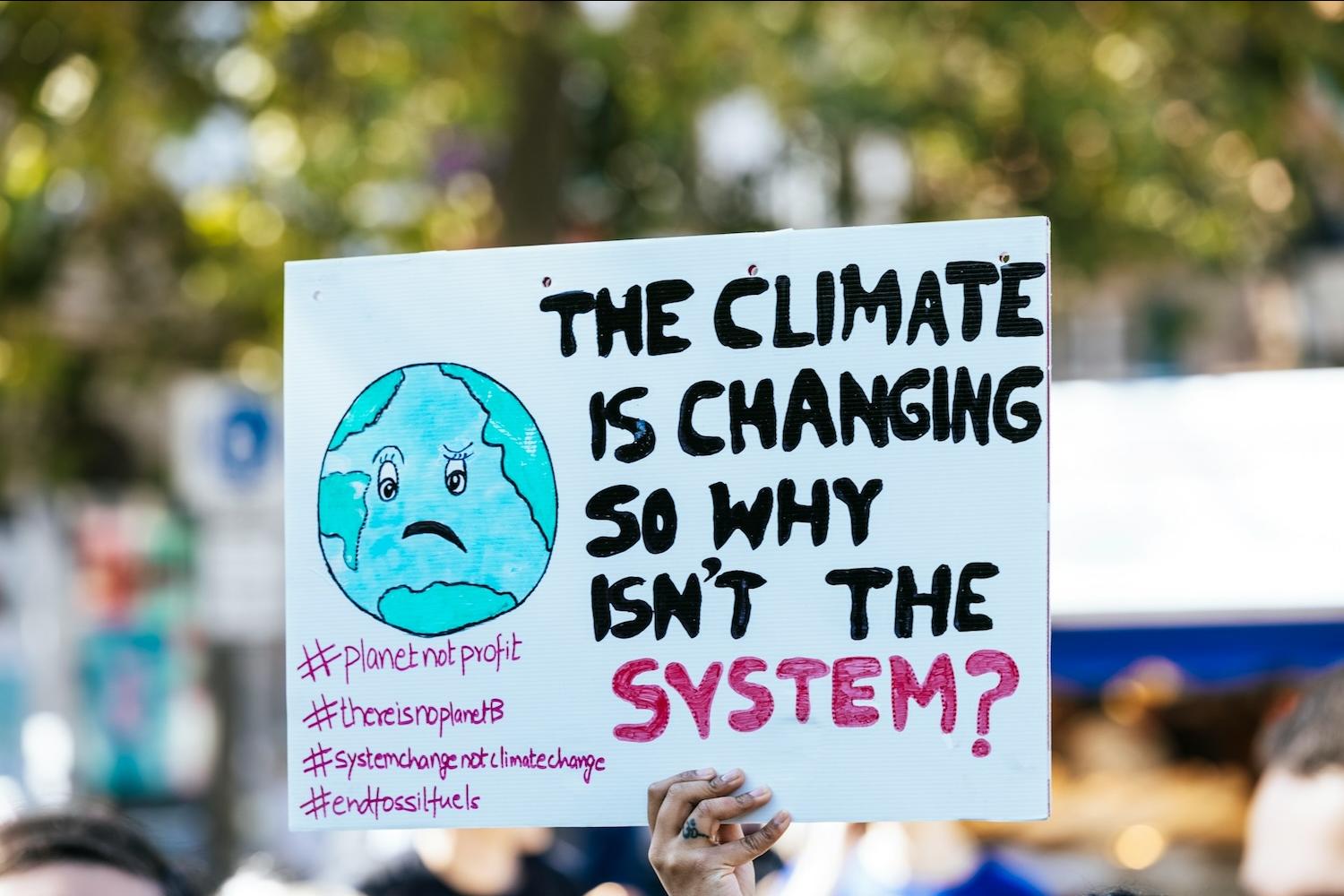 Protestor holding sign that reads The Climate Is Changing So Why Isn't the System