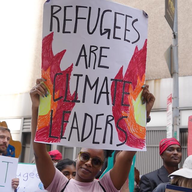 An activist holding a sign that reads "Refugees are climate leaders."