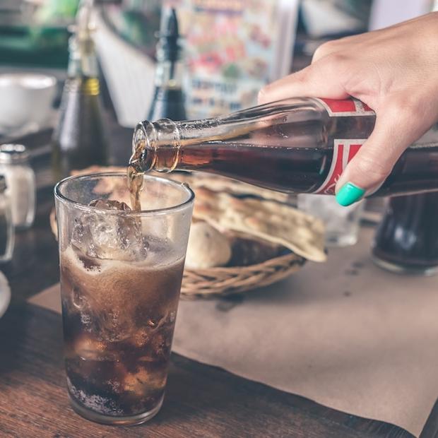 hand pouring coca-cola from a glass bottle at a restaurant table - coca-cola sells billions of beverages in refillable packaging made from plastic and glass globally