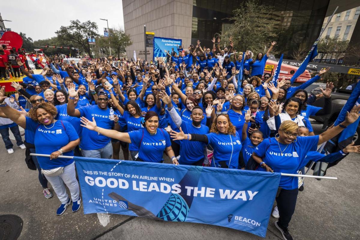 A large group of people wearing blue stand behind a blue parade banner with the words, "good leads the way" 