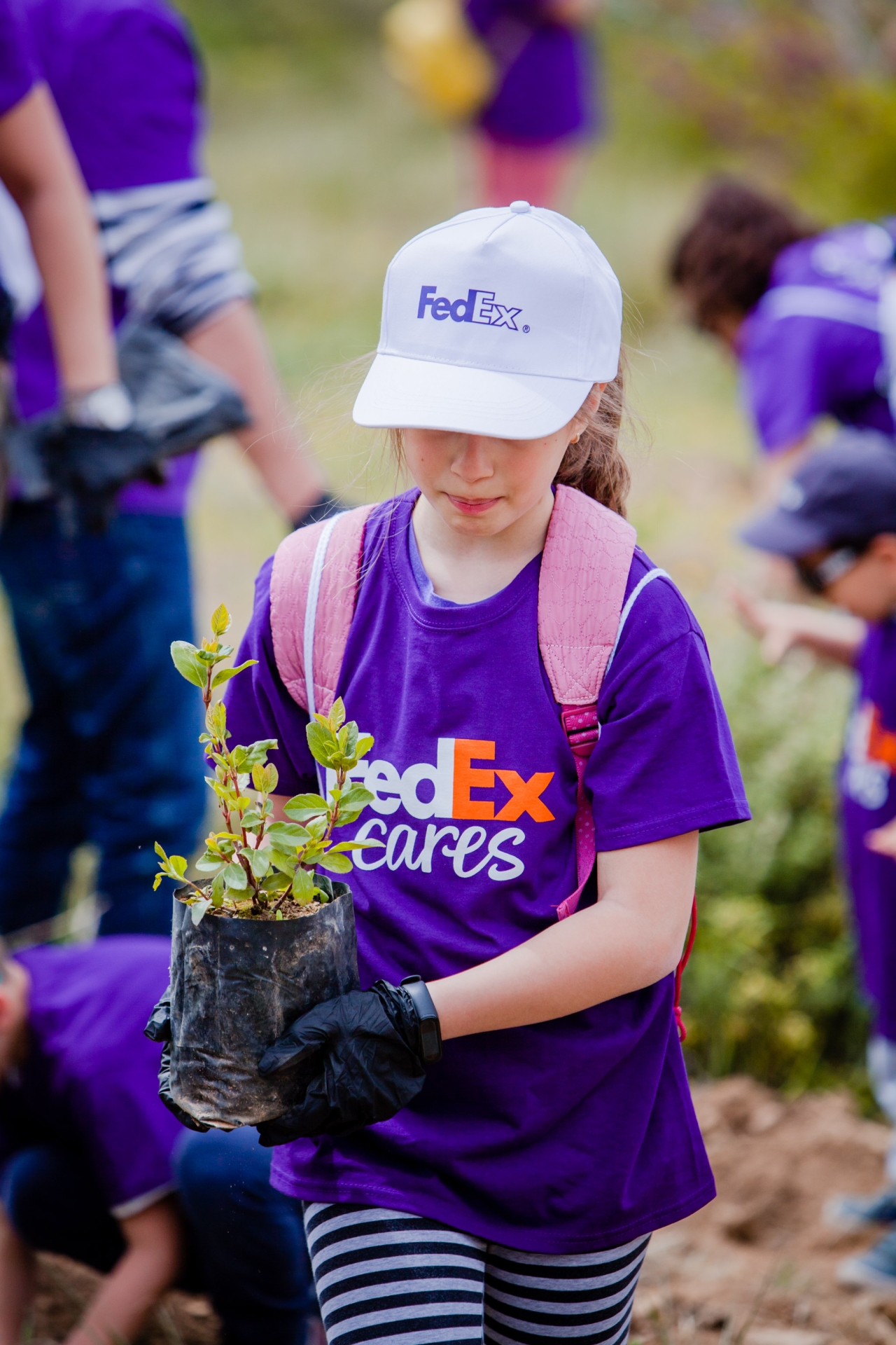 Child wearing a FedEx t-shirt and carrying a plant