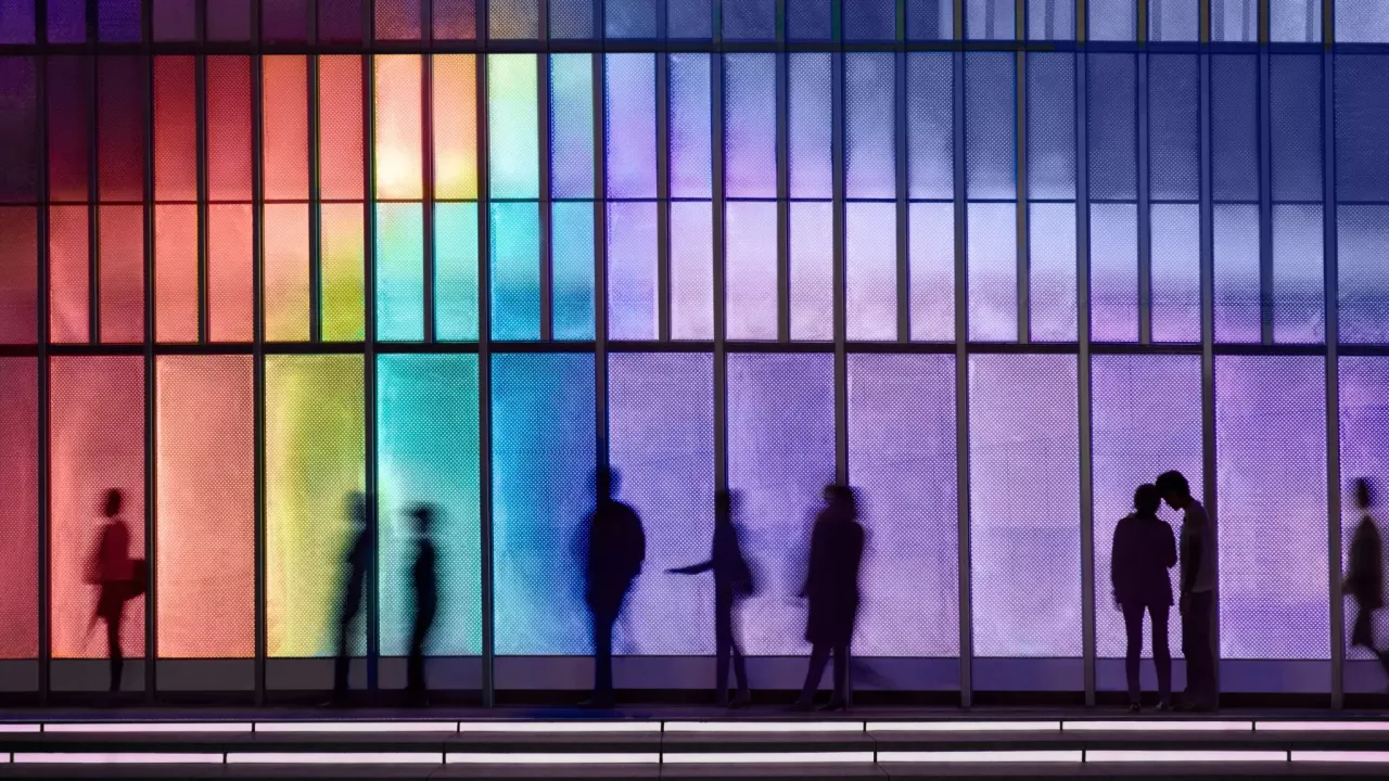 Silhouettes of people behind rainbow colored glass.
