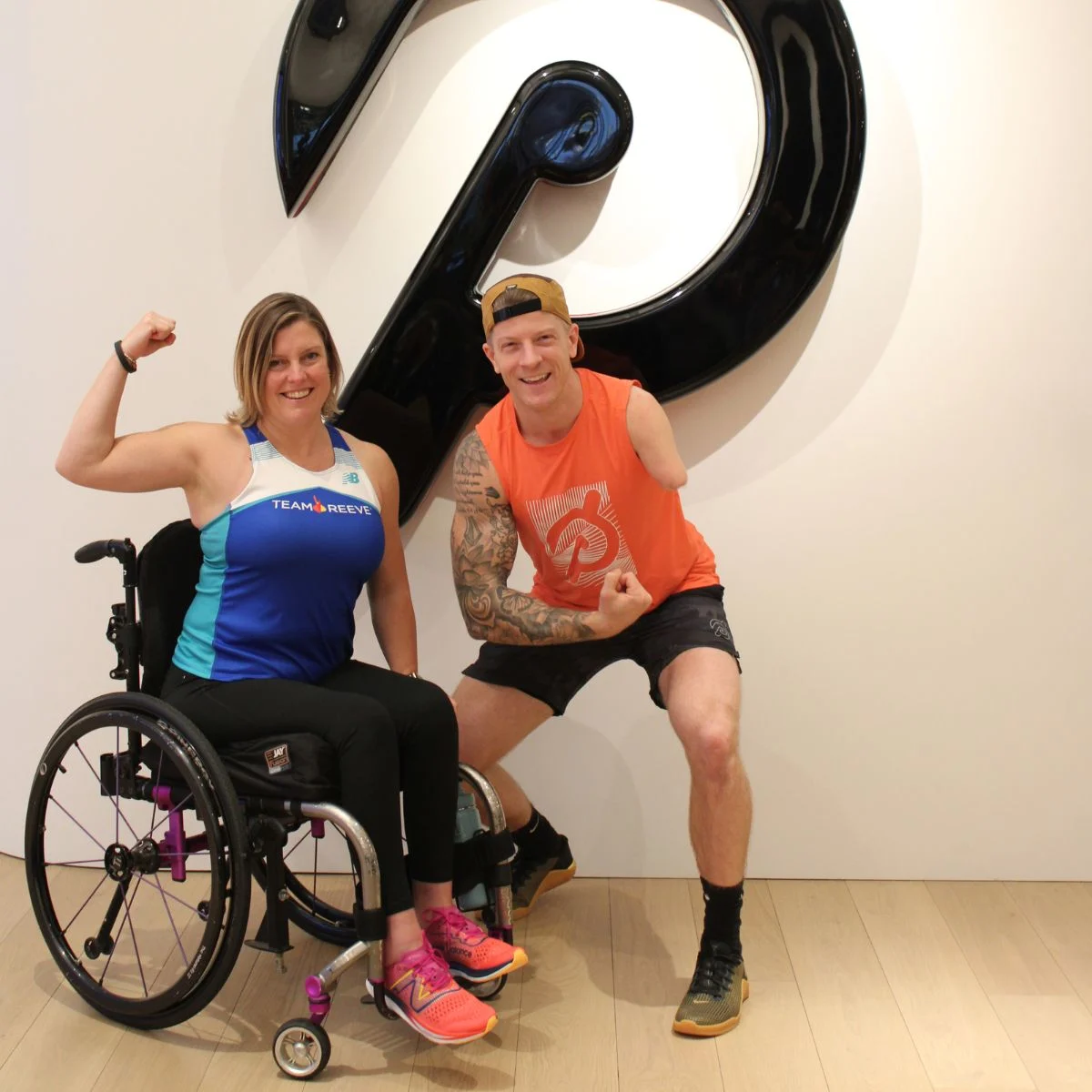 2 people flexing in front of the Peloton logo