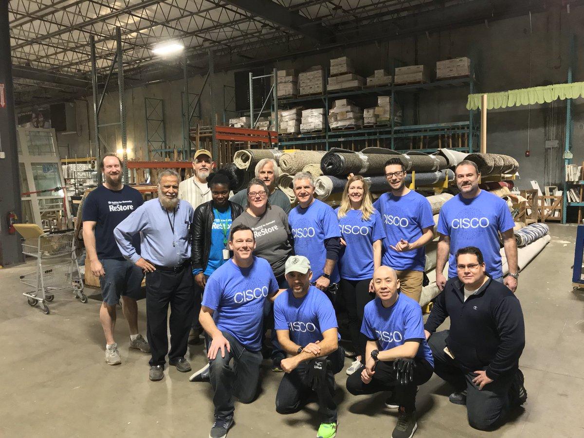 A group of people posed in a warehouse, many wearing matching Cisco t-shirts.