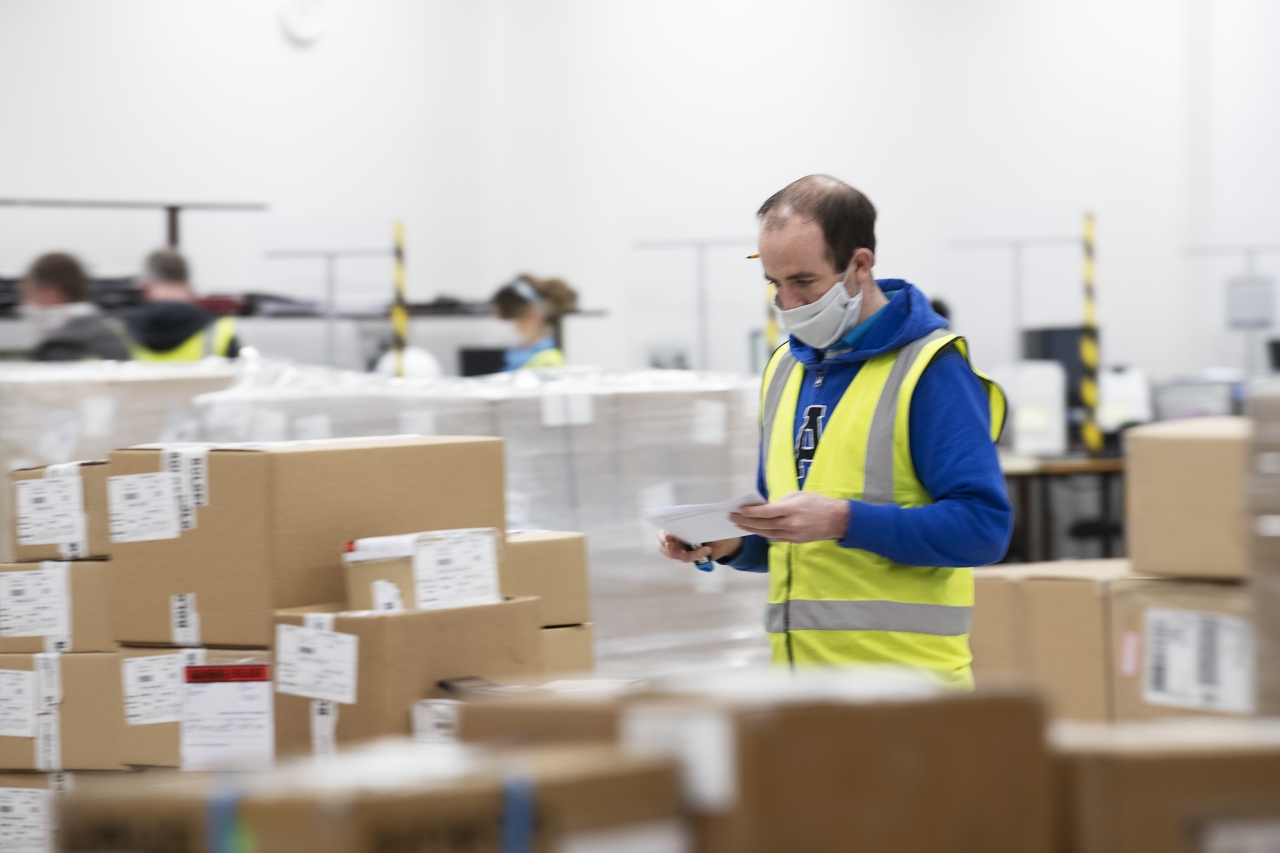Person wearing safety vest walking through piles of packages