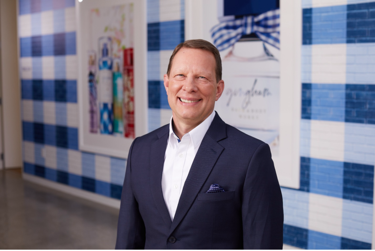 Jeff King stands smiling at the camera in front of a wall painted with a blue and white gingham pattern at Bath & Body Works’ home office in Columbus, Ohio.