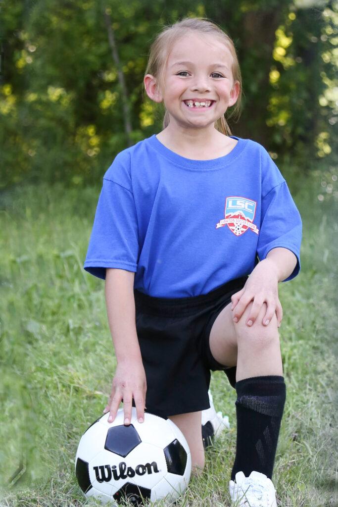 A child kneeling on grass with their hand on a soccer ball