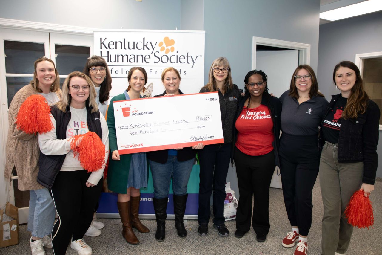 People standing together inside, two of them holding a large check