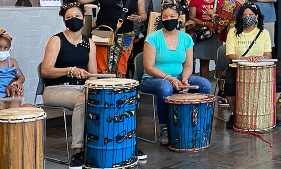 museum-goers in masks sitting behind drums of different colors and sizes
