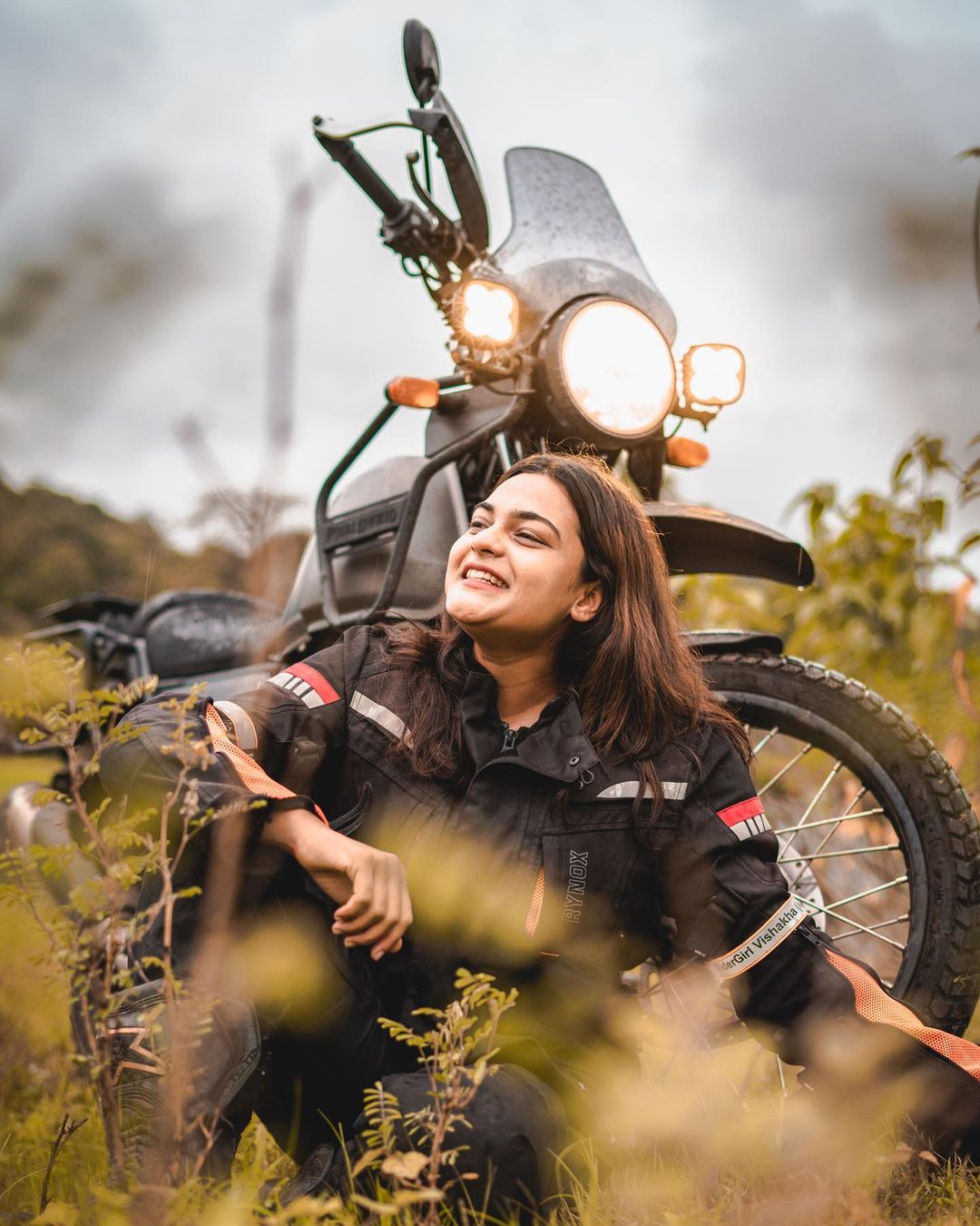 Vishakha Fulsunge in a field, sitting in front of her motorcycle