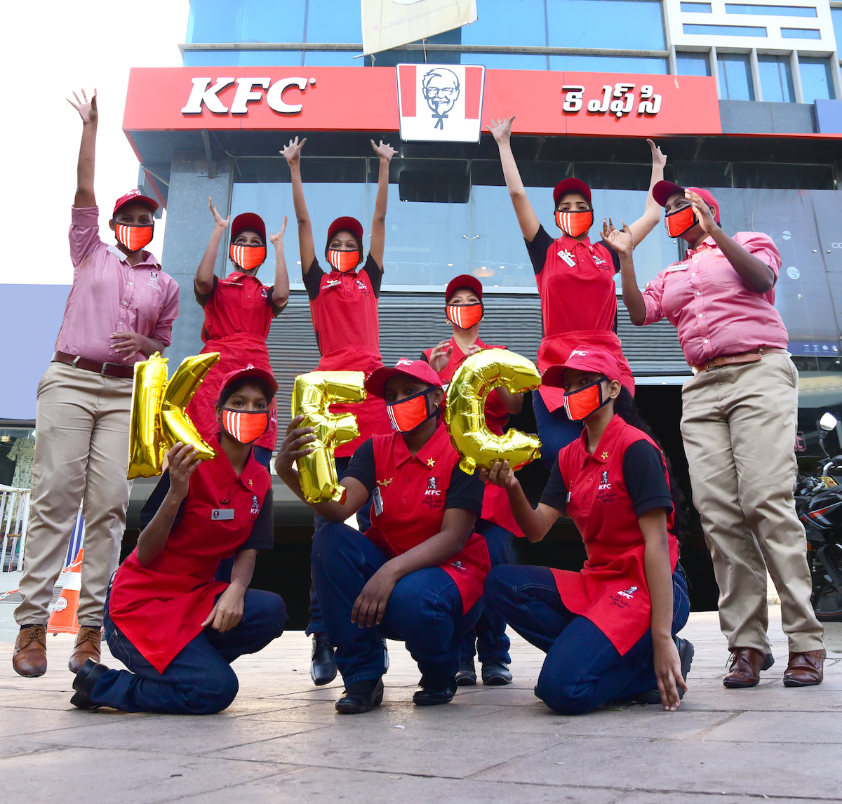 Workers celebrate in front of newly opened KFC, holding balloons that read "KFC"