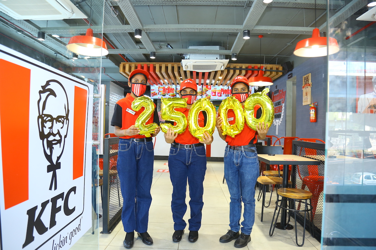 Workers standing inside new KFC location hold balloons reading "25,000"