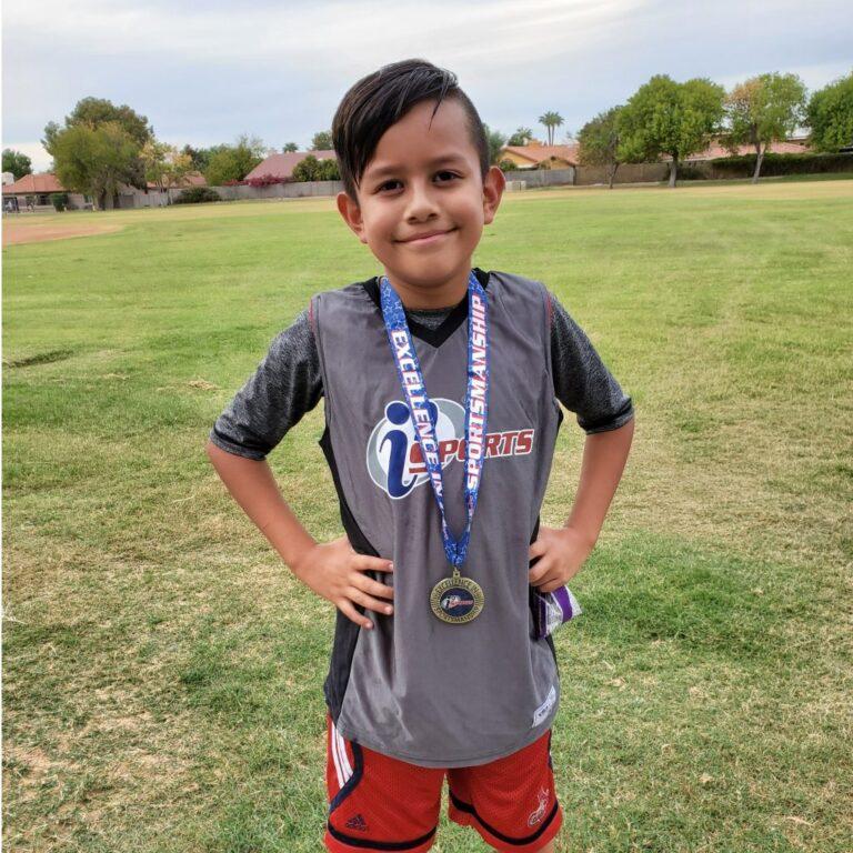 A child standing in a field smiling, with an award medal around their neck