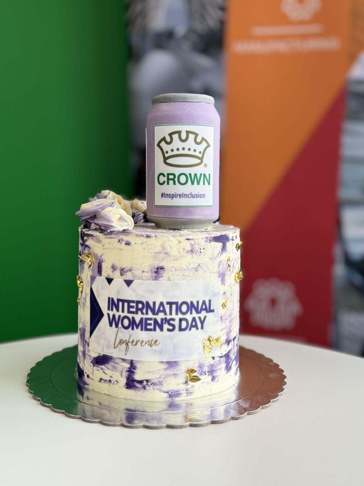 A white and purple cake that has "international women's day conference" on the front 