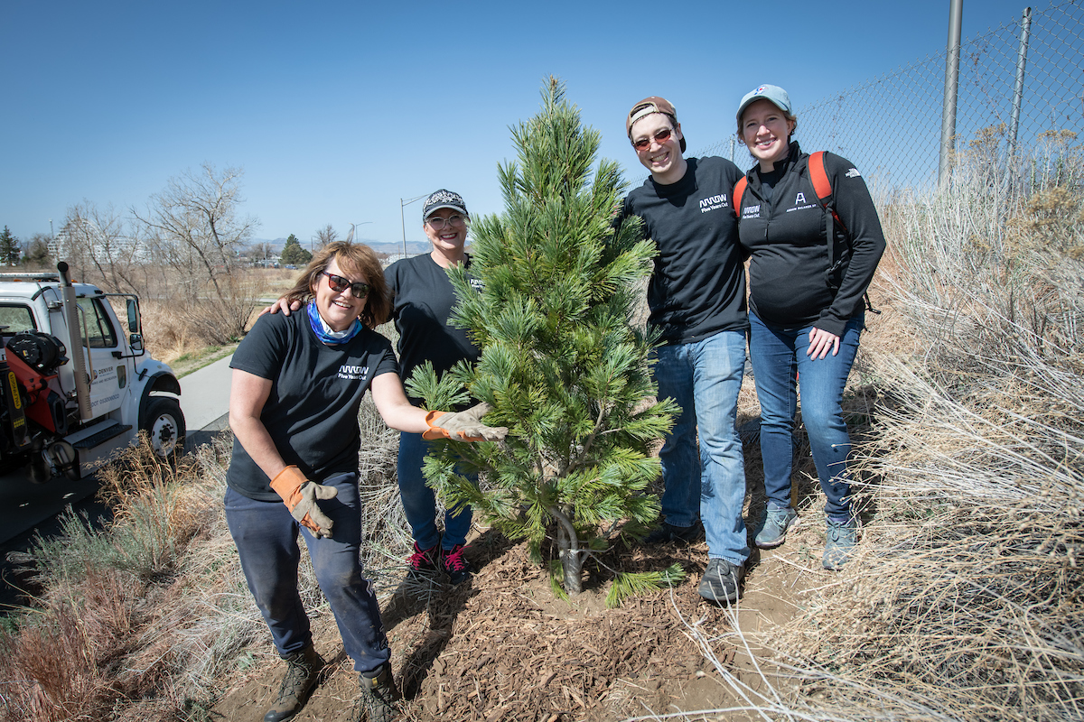 Arrow employees pose next to a planted tree on Earth Day 