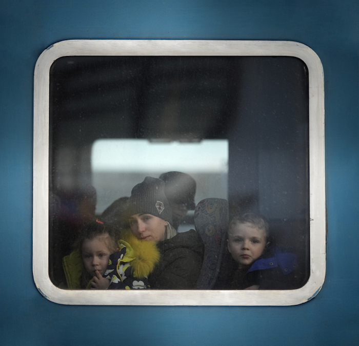 A mother and her children seated in a train and looking out the window.