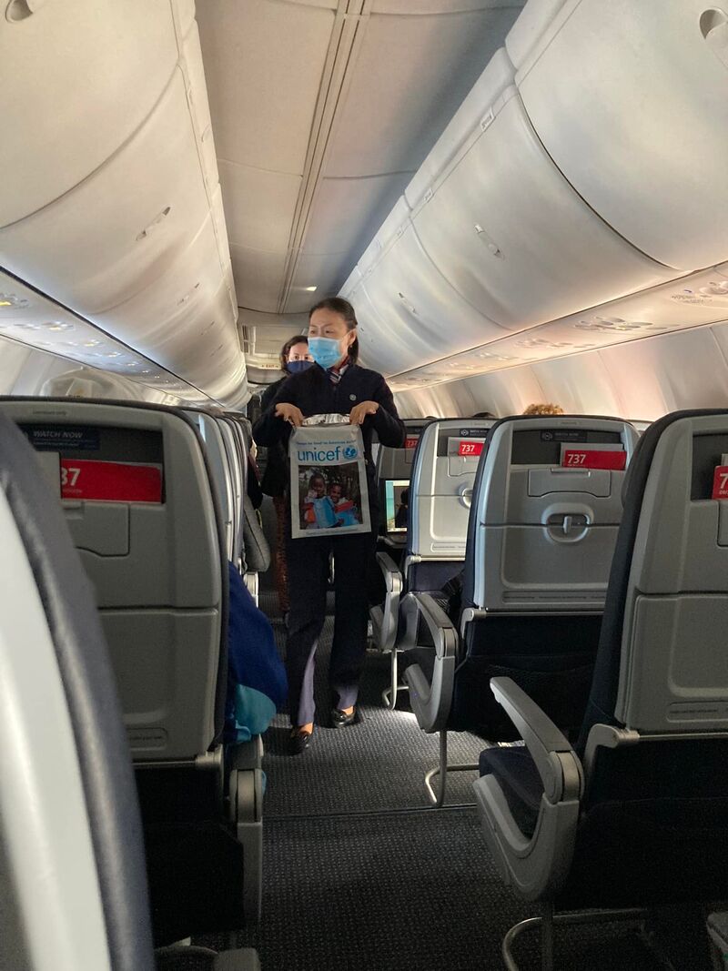Flight attendant walking down an airplane aisle holding a UNICEF donation bag