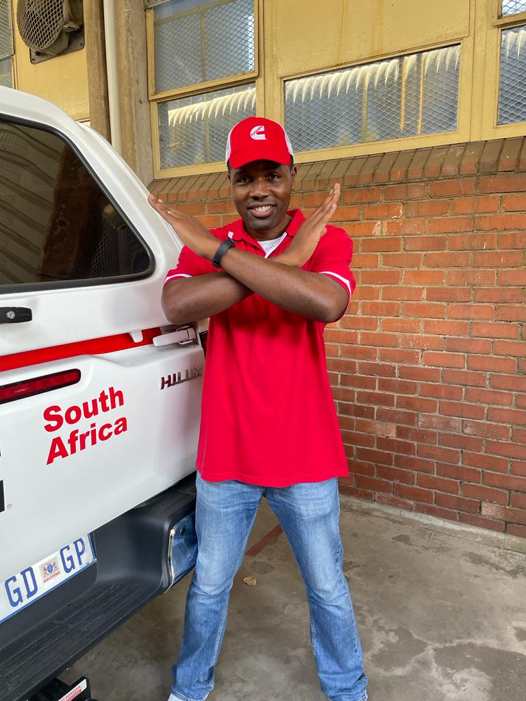 Man in a red shirt next to a van that says South Africa, crossing his arms