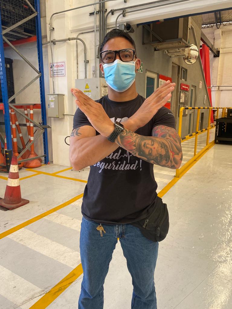 Man wearing a surgical mask and glasses in an industrial setting, crossing his arms