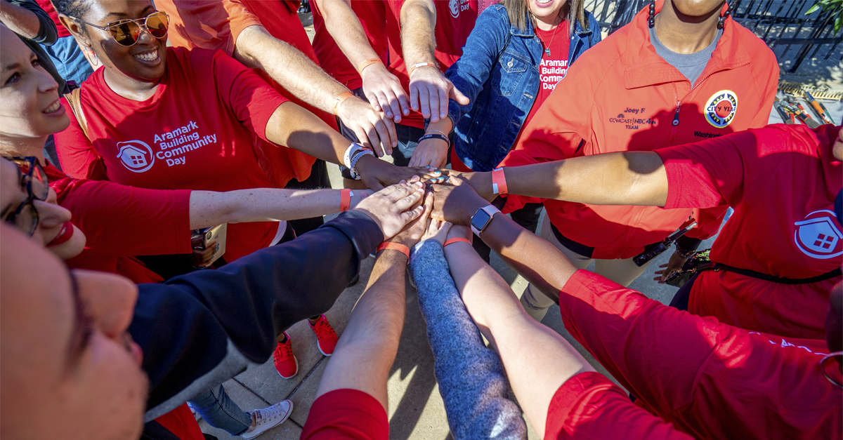 Aramark volunteers join their hands together in the center of a circle as part of a team huddle