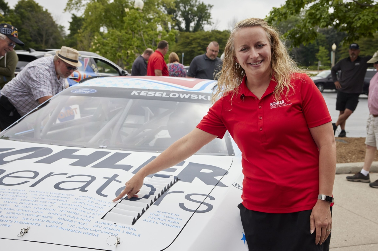 a person stands by a car and points to a name on the hood