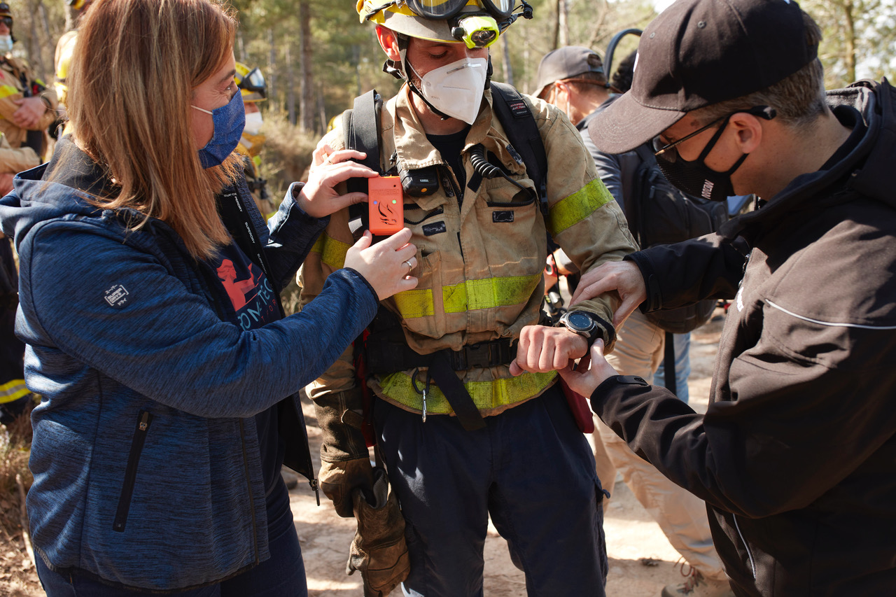 two people assisting a firefighter, checking their devices 