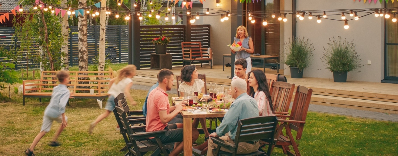 a group of people sitting at an outside dining table. Children running in the background