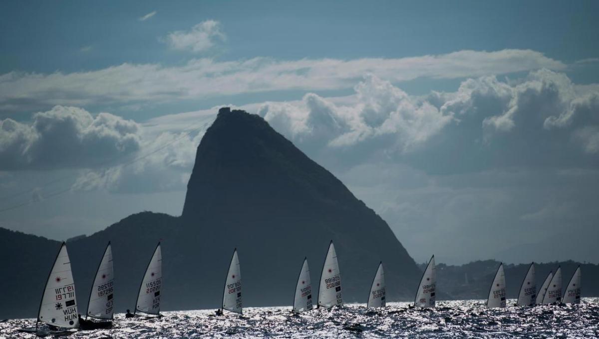 sailboats in the water in front of a dramatic mountain with clouds in the distance