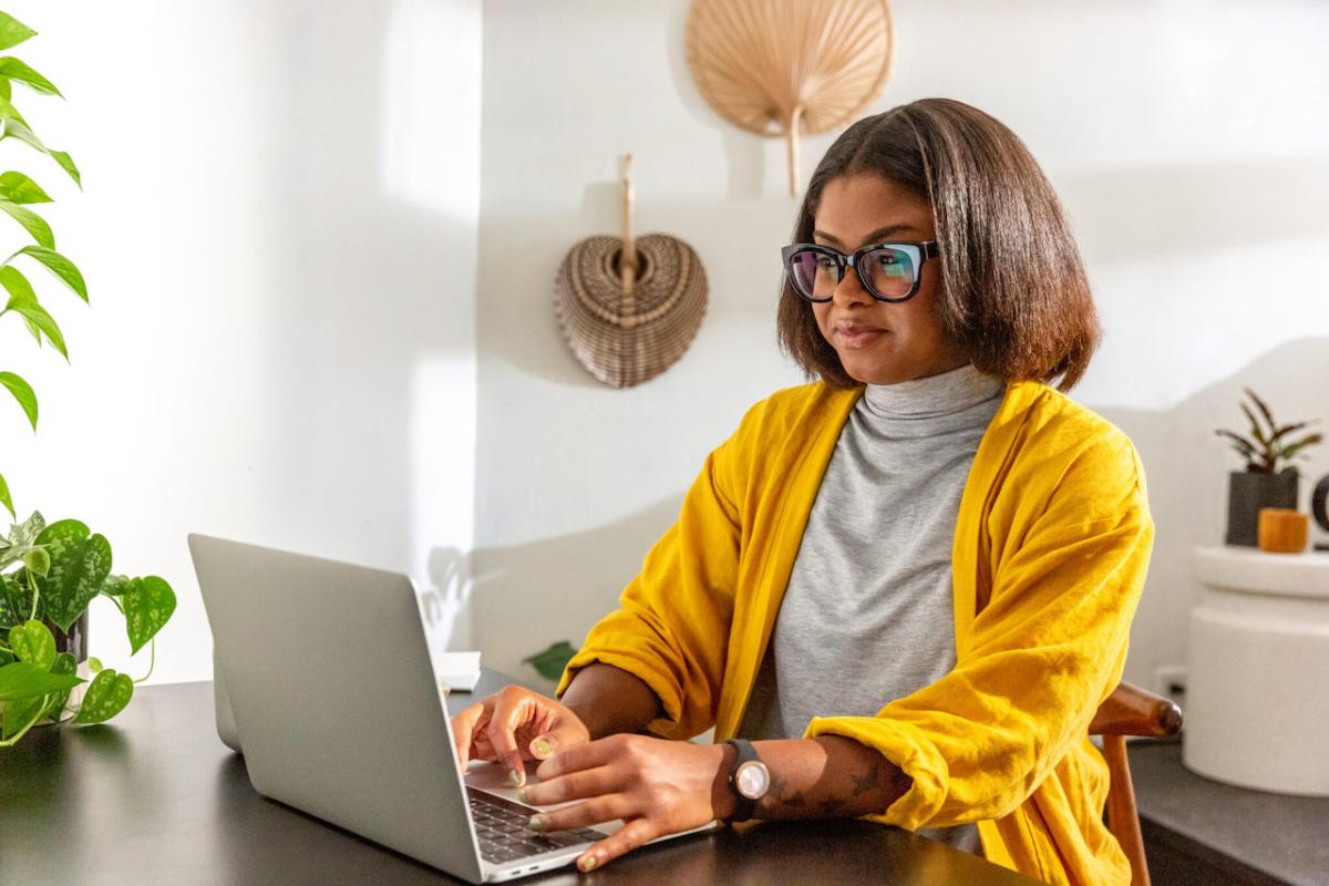 Black woman seated at a table and working on her laptop.