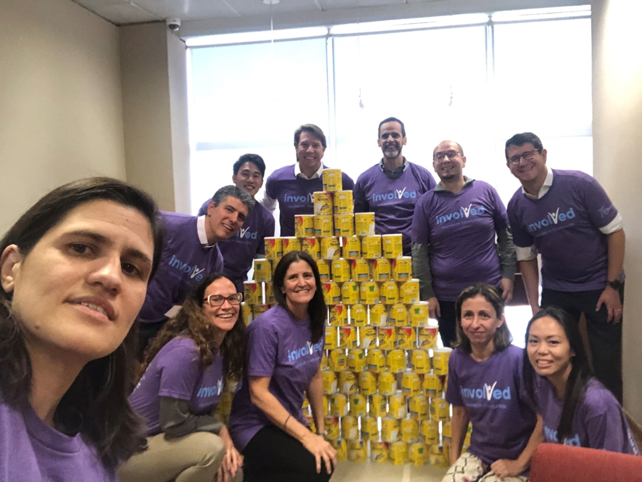 Group wearing "Involved" T-shirt and posing by a pyramid of cans