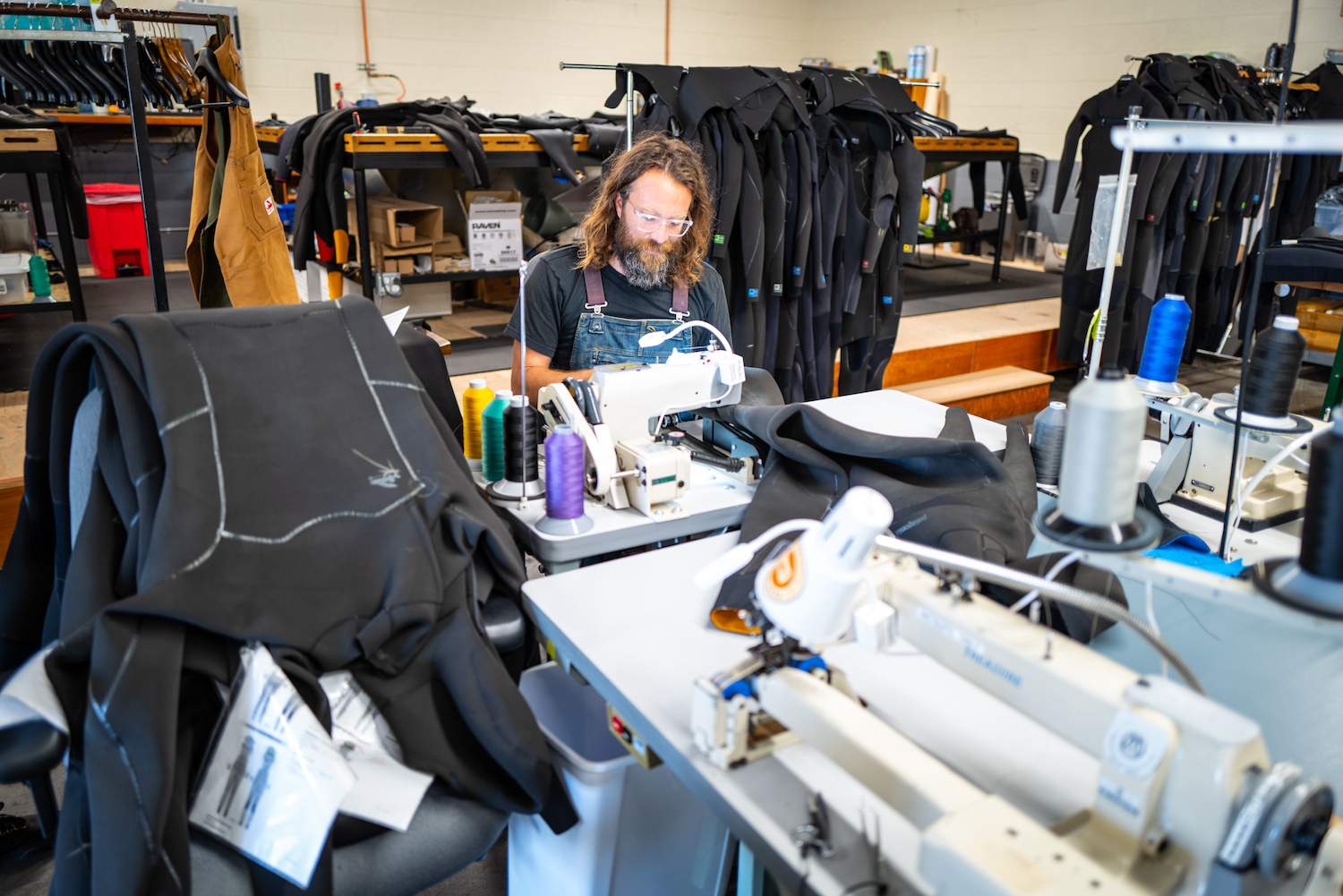 A person sits at a sewing machine repairing wetsuits. 