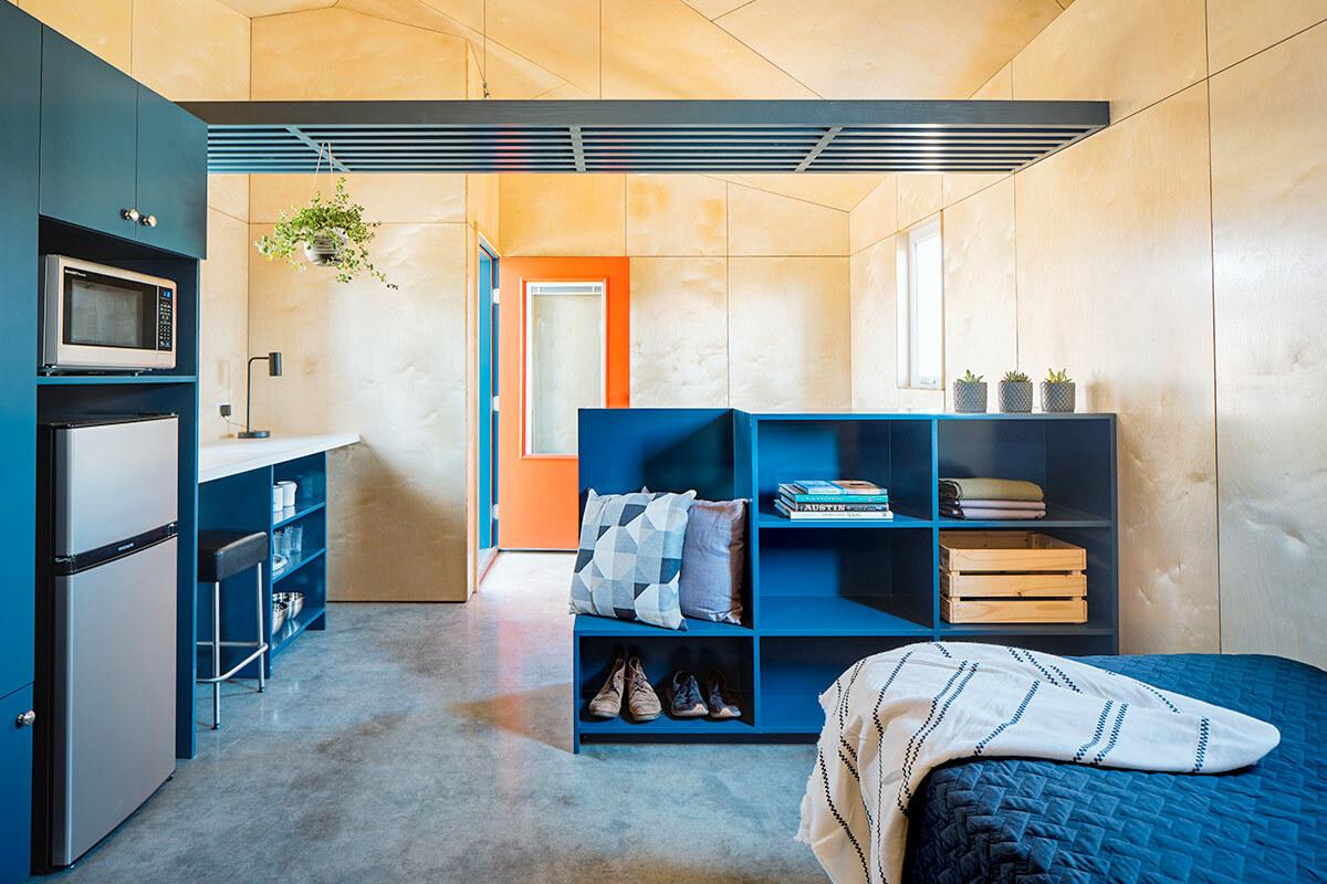 interior of a tiny home. A single bed, bookcase, refrigerator and microwave.