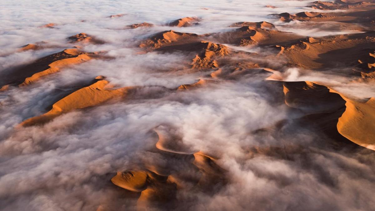 Panoramic landscape of low clouds over desert sands and hills.