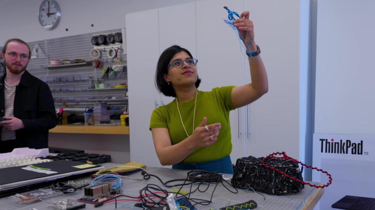 A person in a workshop, holding up some blue wire