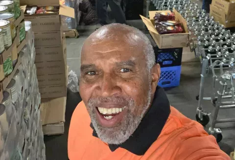 Calvin taking a selfie next to pallets of canned foods in a storage room.