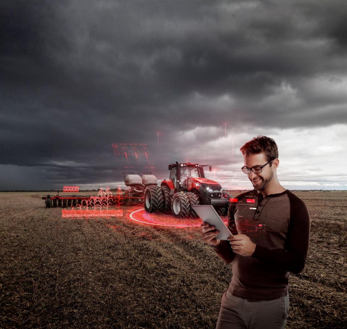 Red agricultural equipment in a crop field, with a person stood looking at a tablet PC