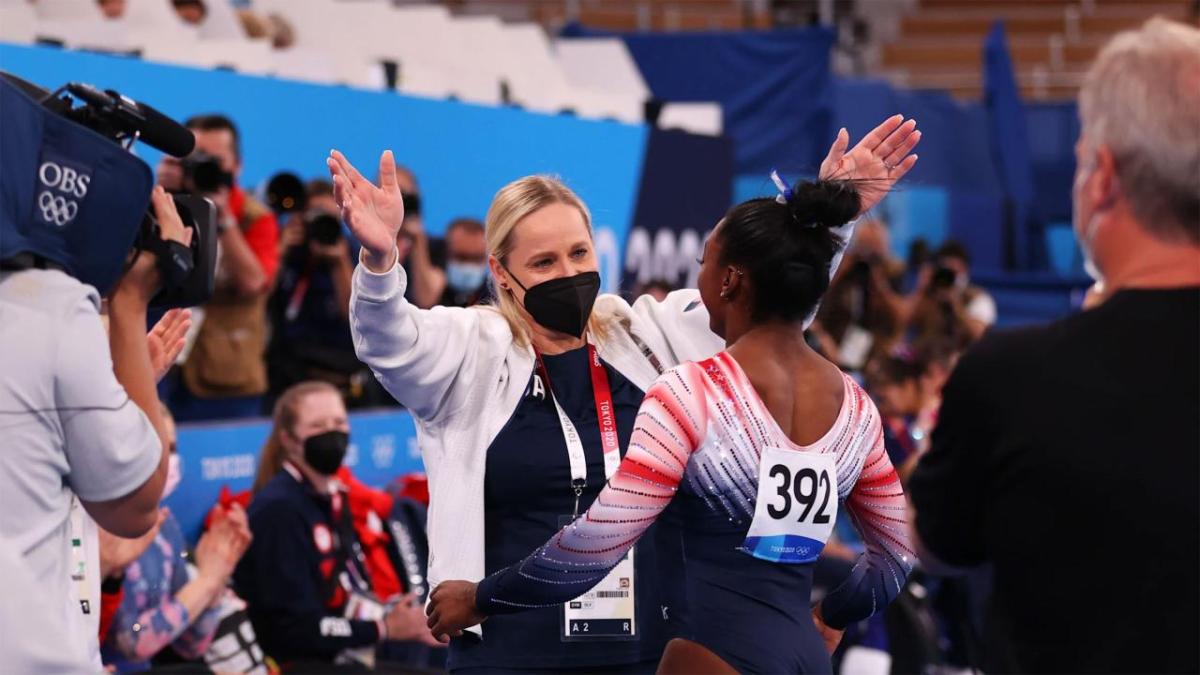 Cici and Simone Biles with arms out for a hug, reporters and spectators around them