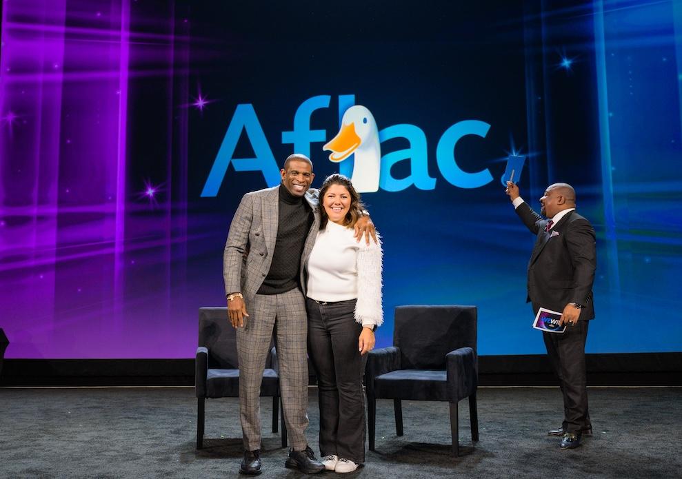 Coach Prime and Jaime Gaudet shown on stage with the Aflac logo.