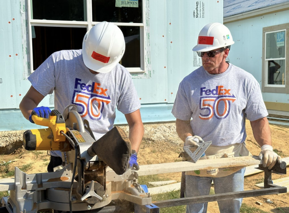 Two people using machinery to cut wood outdoors