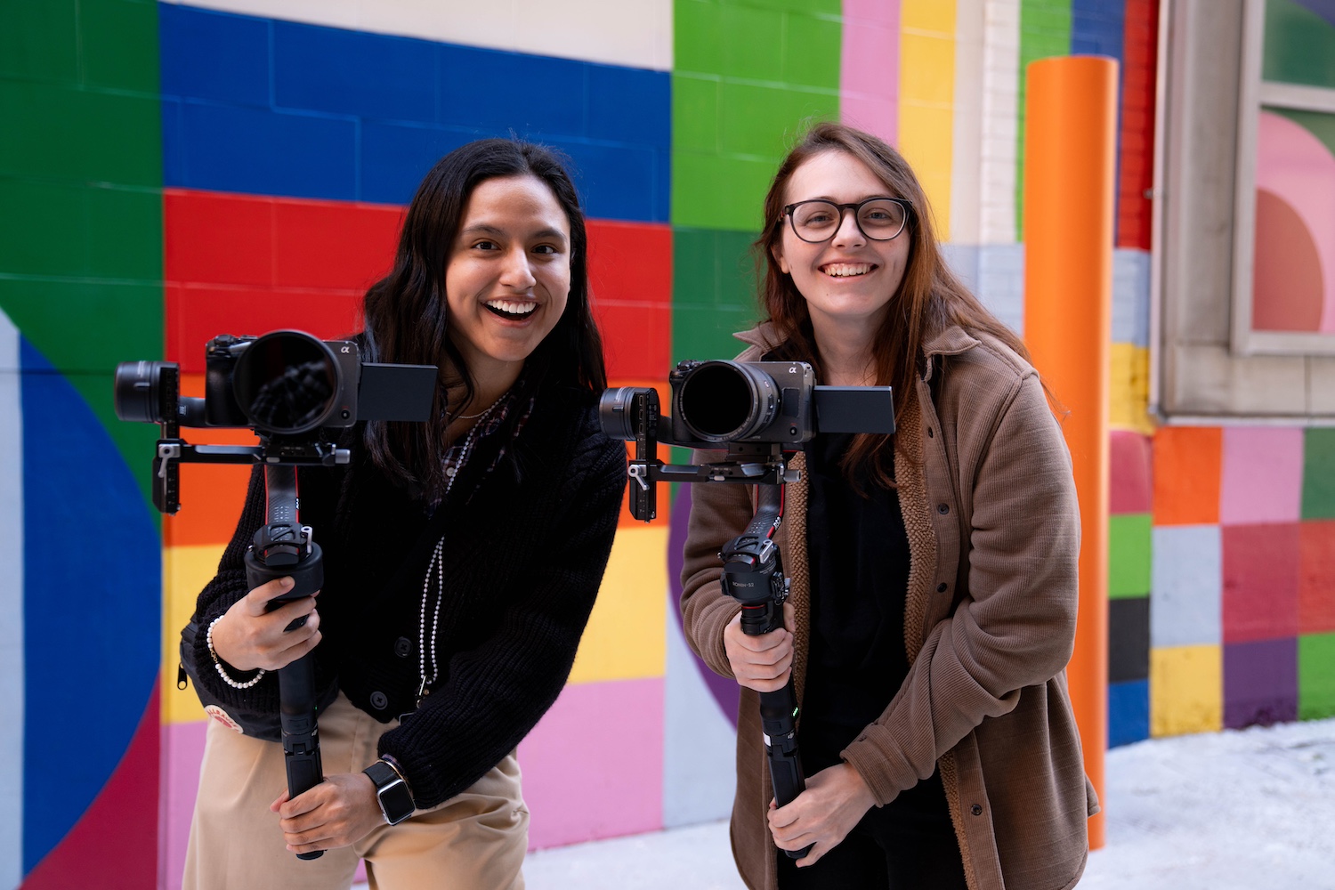 Two Creative Impact Lab participants smile while holding cameras. 