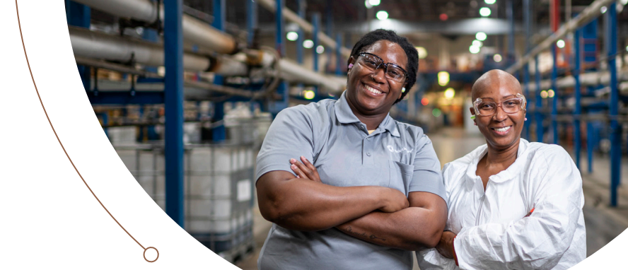 Two smiling people with arms crossed in a manufacturing environment.