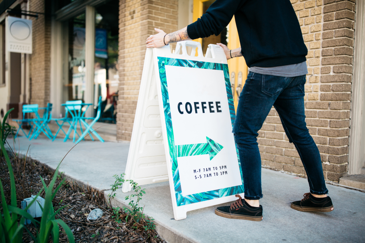 Person shown adjusting a sign in front of a coffee shop.