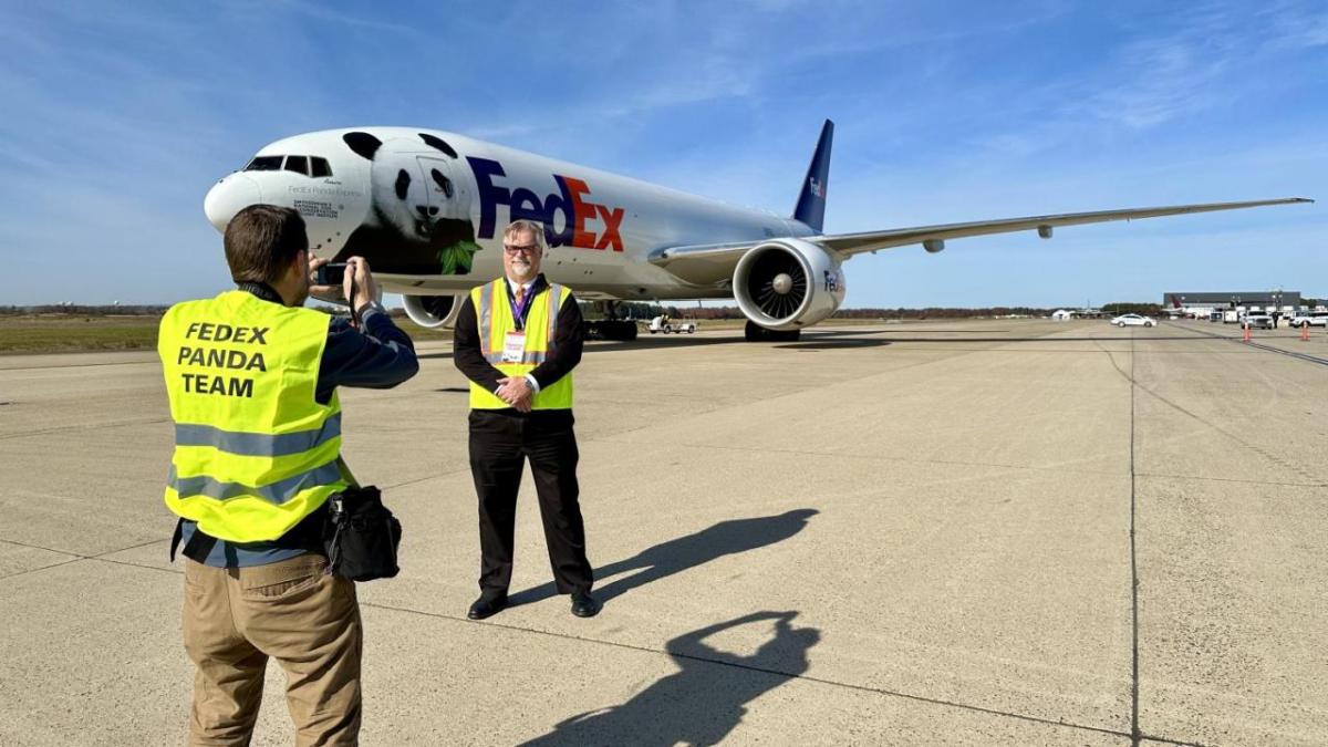 Dave Lange being photographed standing outside in front of a FedEx plane.