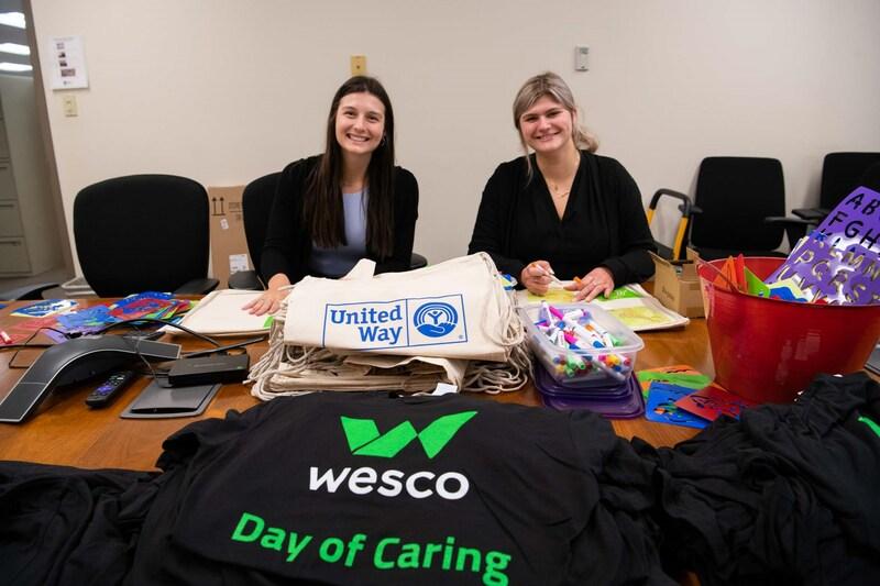 Two people at a table with Wesco Day of Caring shirts on it