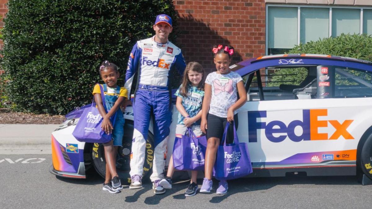 Denny Hamlin with children in front of a race car.