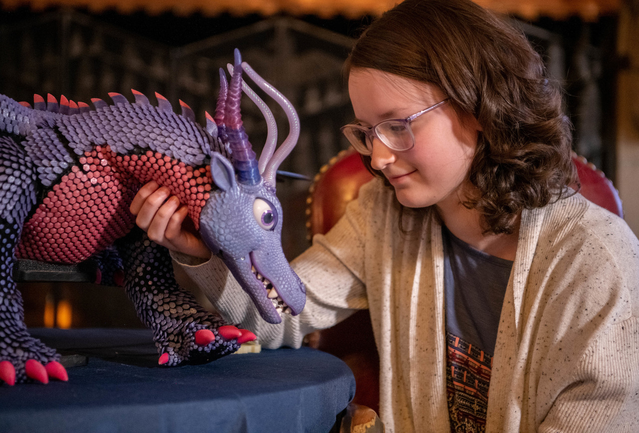 Belle petting her dragon robot made by Arrow and Make-A-Wish Colorado
