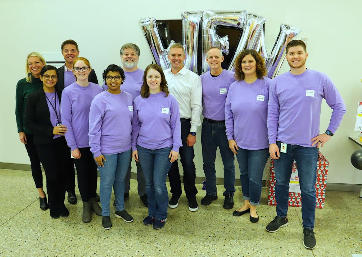 A group of people posed, most in matching purple shirts.