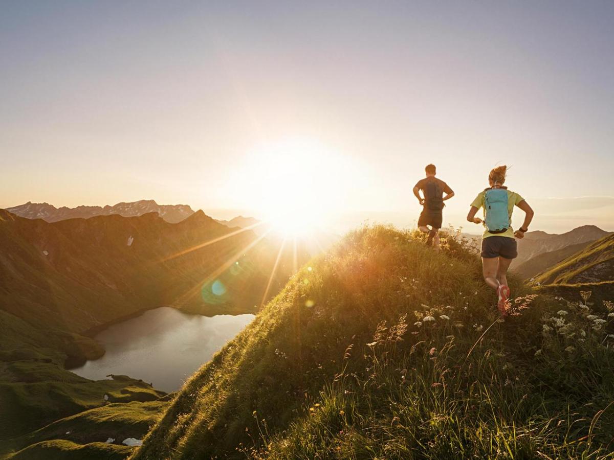 Photo of the sun setting with two people running on some hills 