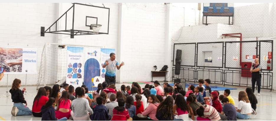 Person stood in a hall giving a presentation to students who are sat on the floor in front of them