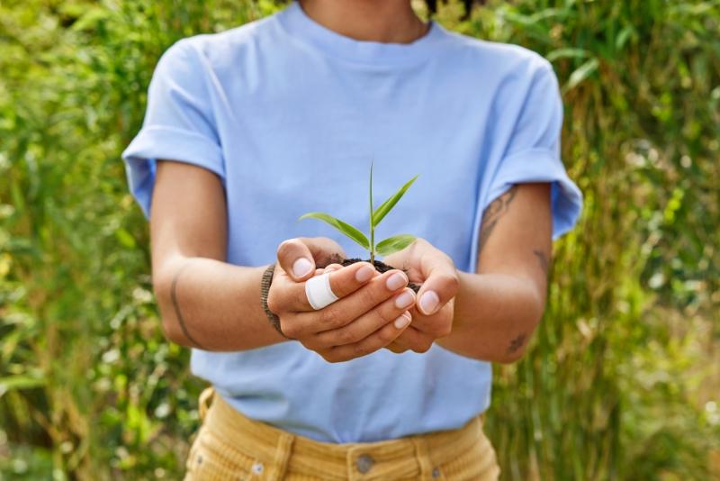 Young woman holding a small plant in her hands.